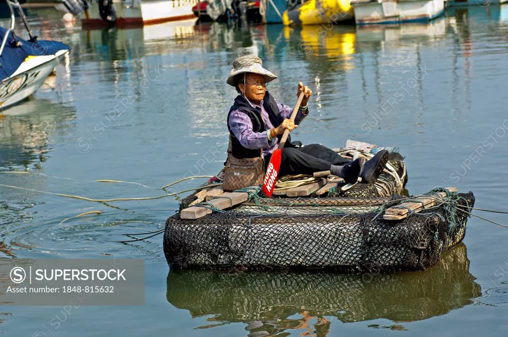 Older woman paddling over a canal in a makeshift raft, Sai Kung, Hong Kong, China