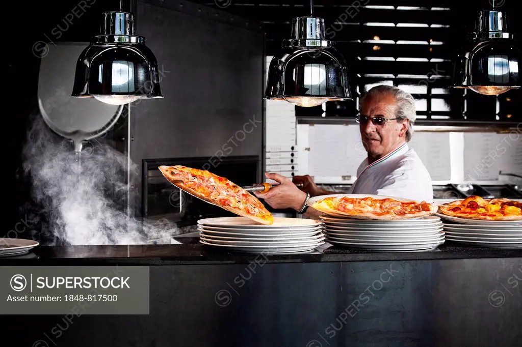 Pizza baker taking the finished pizza out of the oven with a pizza shovel