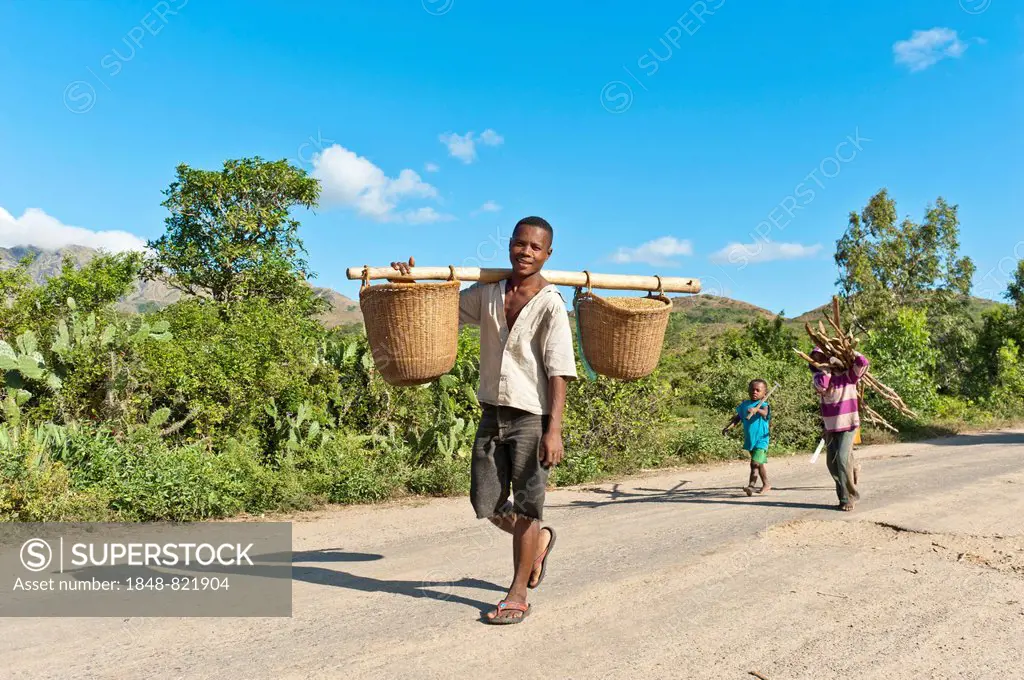 Man of the Antandroy people carrying two baskets on a wooden pole, on a street near Fort Dauphin or Tolagnaro, Madagascar