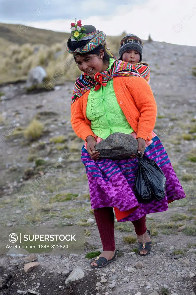Young woman with child in a sling carrying a heavy stone to secure the shores of an artificial lake for irrigation, Quispillacta, Ayacucho, Peru