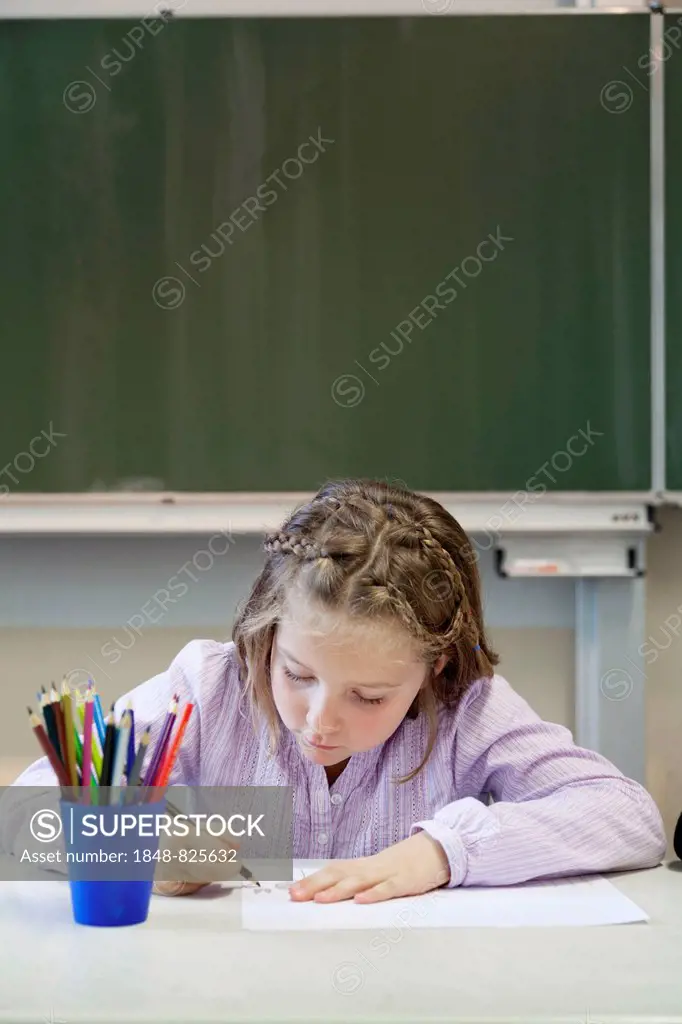 Schoolgirl, 7 years, painting a picture in front of a blackboard