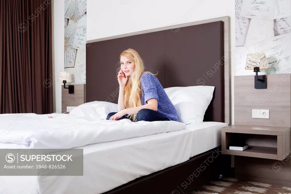 Woman sitting with her laptop on the bed in a hotel room
