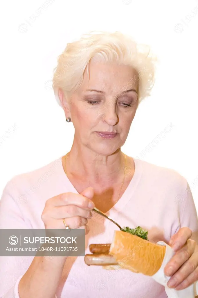 A woman putting parsley on a sausage in a baguette