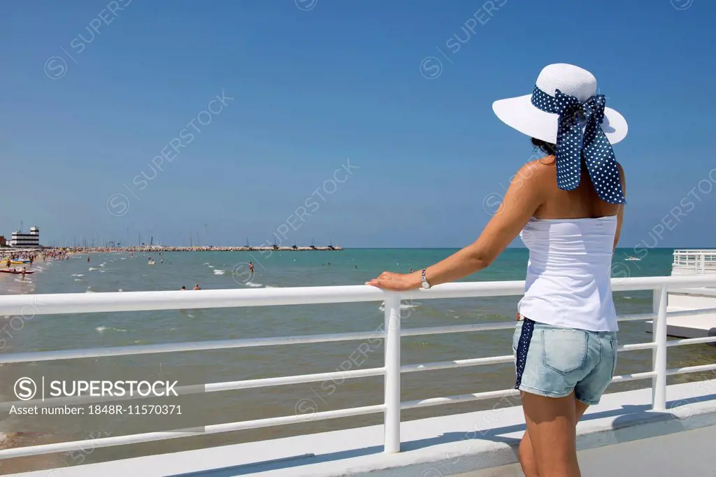 Woman with hat standing at railing on the beach, Adriatic, Senigallia, Province of Ancona, Marche, Italy