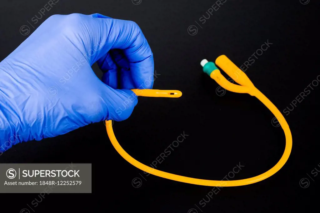 A hand with a blue medical glove is holding a balloon catheter