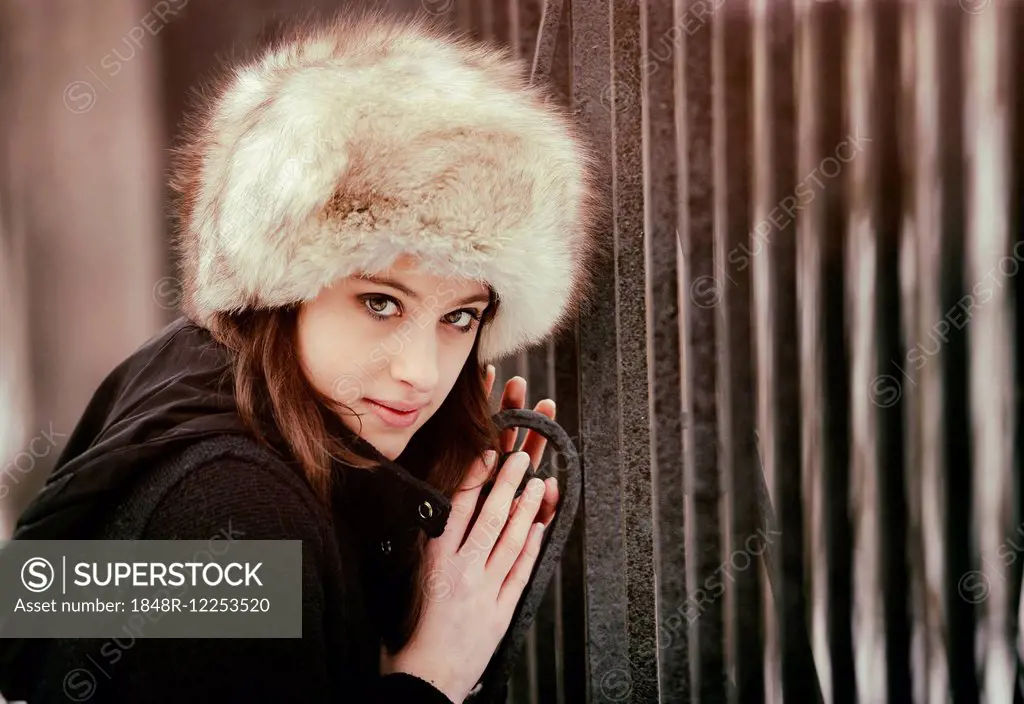 Young woman wearing a fur hat, at a gate in winter