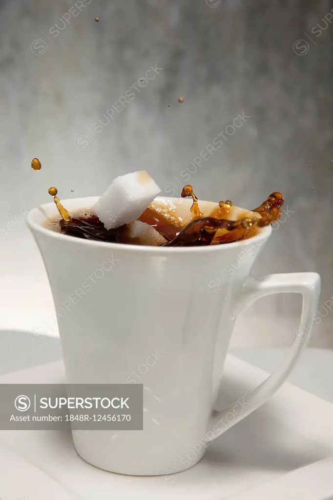 Two sugar cubes falling into a cup of coffee