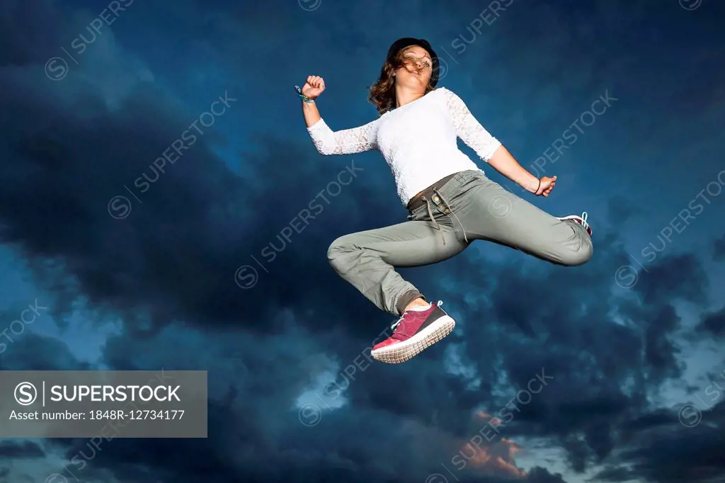 Young woman, 19 years old, jumping, in mid-air, against the evening sky