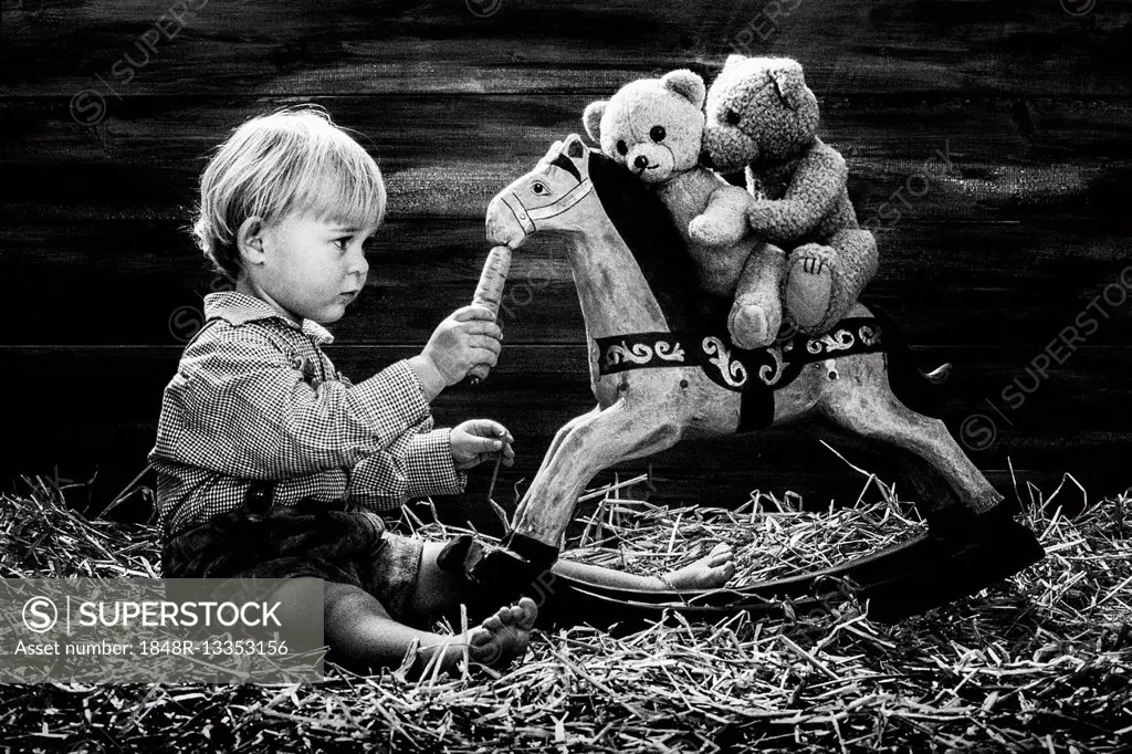 Three-year-old girl feeding rocking horse, teddy bears riding, Austria