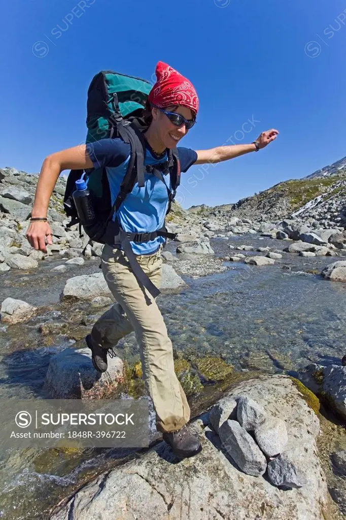 Young woman jumping across a creek, hiking, backpacking, hiker with backpack, historic Chilkoot Trail, Chilkoot Pass, near Crater Lake, alpine tundra,...