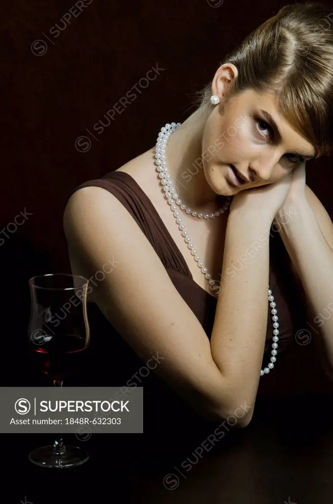 Young woman wearing a pearl necklace and pearl earrings, beside red wine in a wine glass