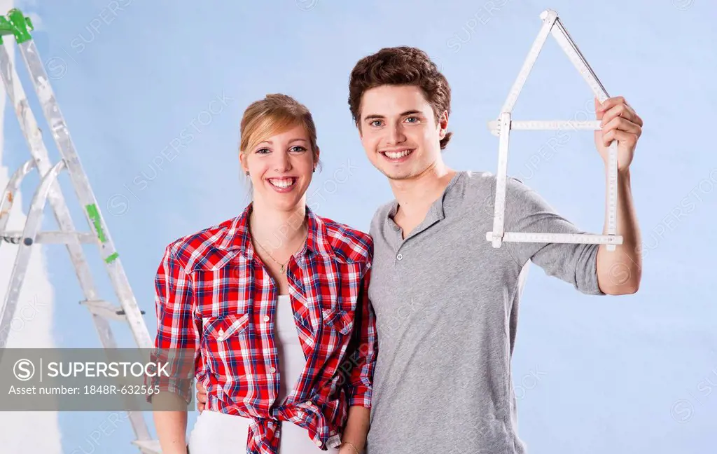 Young couple holding a folding carpenter's ruler in the shape of a house