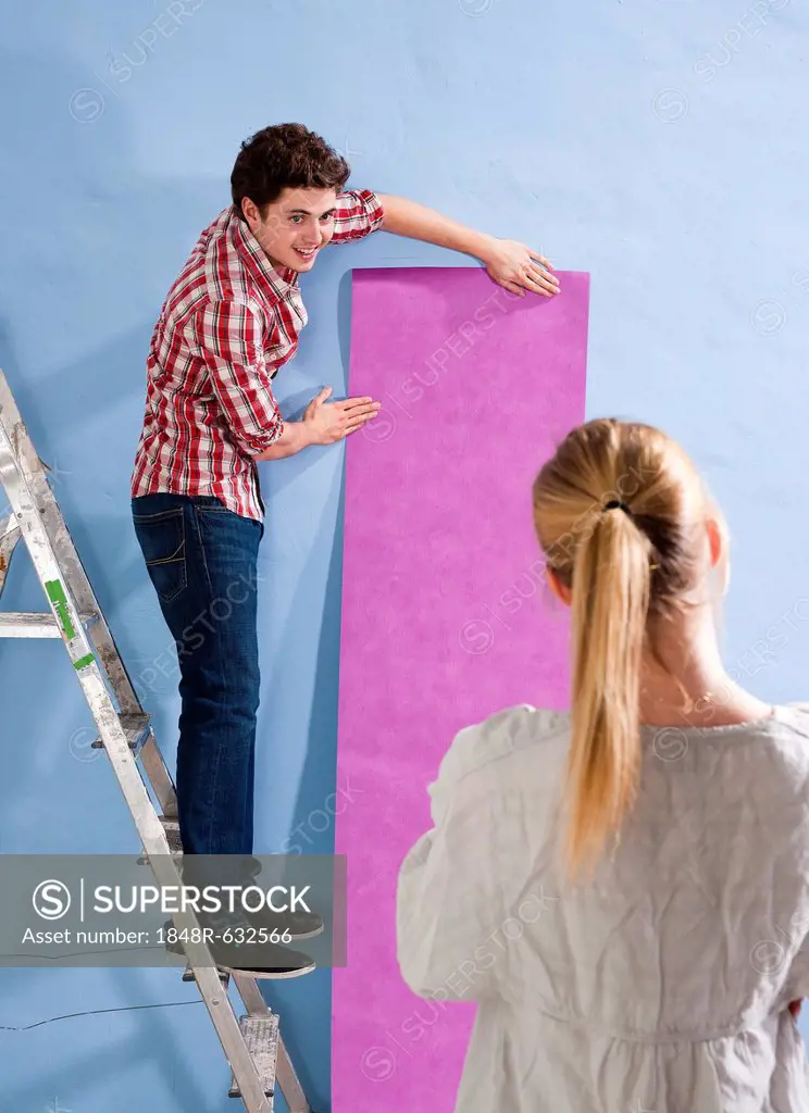 Young couple applying wallpaper to a wall