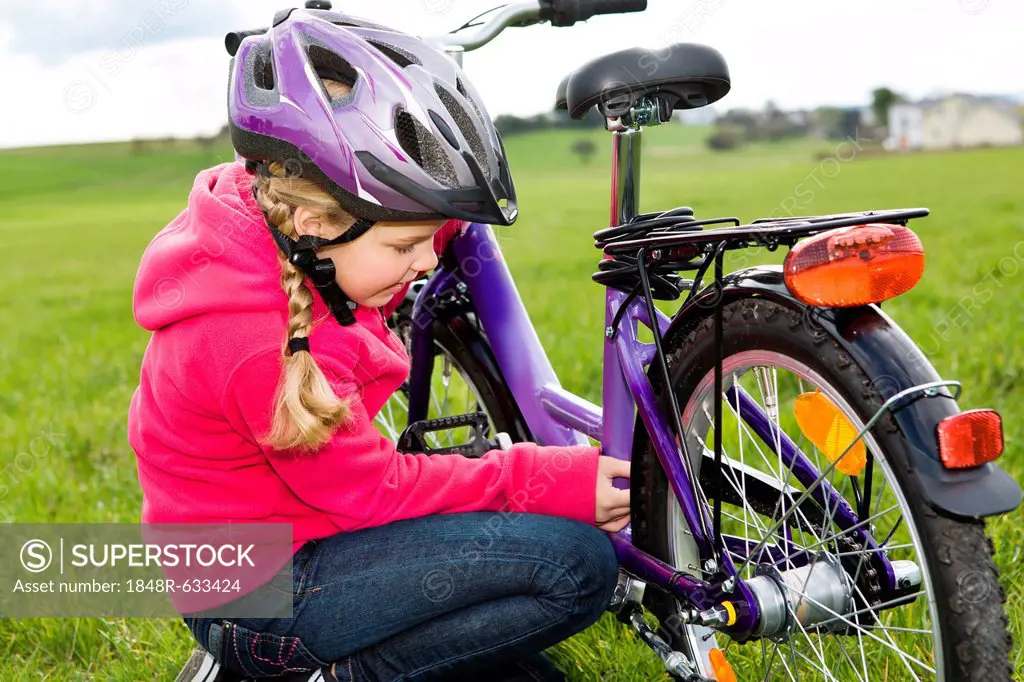Girl wearing a cycling helmet, checking her bicycle