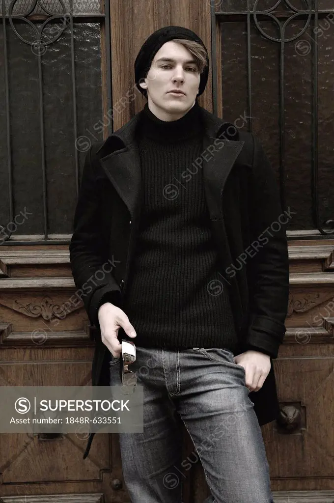 Young man wearing winter clothes, standing in front of a front door