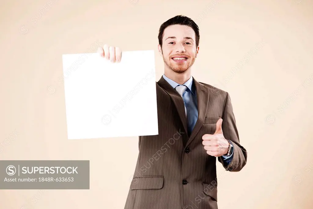 Young man wearing a suit recommending a blank board in his hand with a thumbs-up gesture