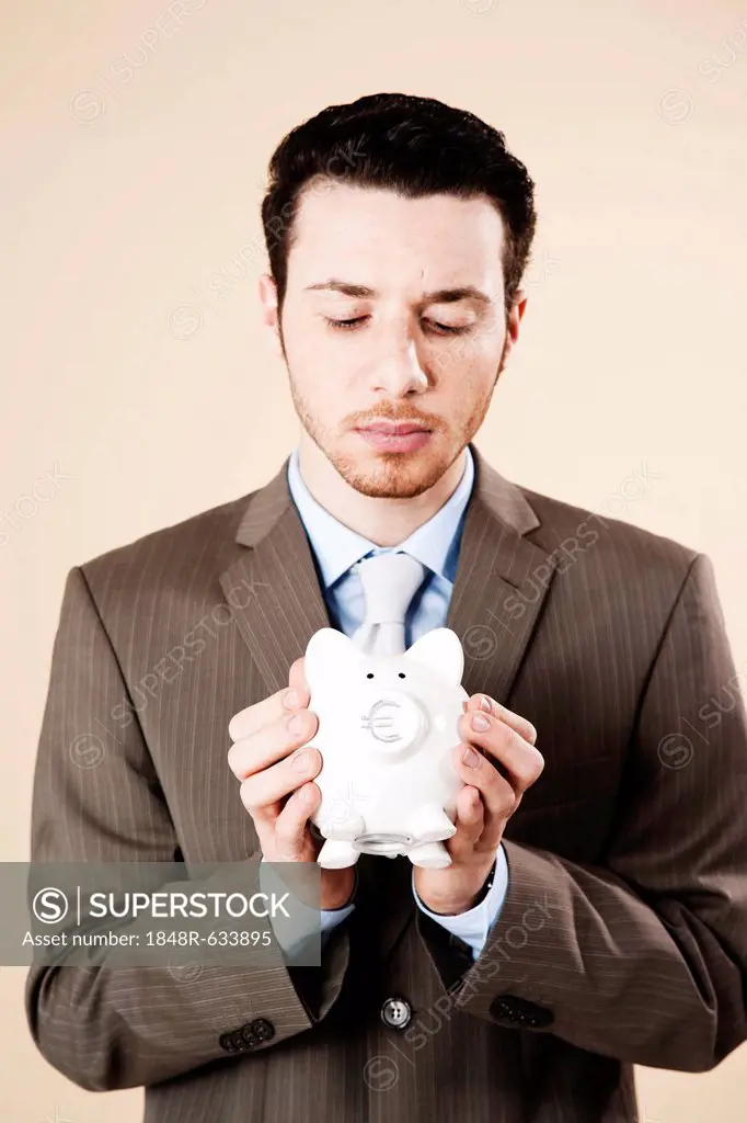 Young businessman with a concerned expression holding a piggy bank in his hands