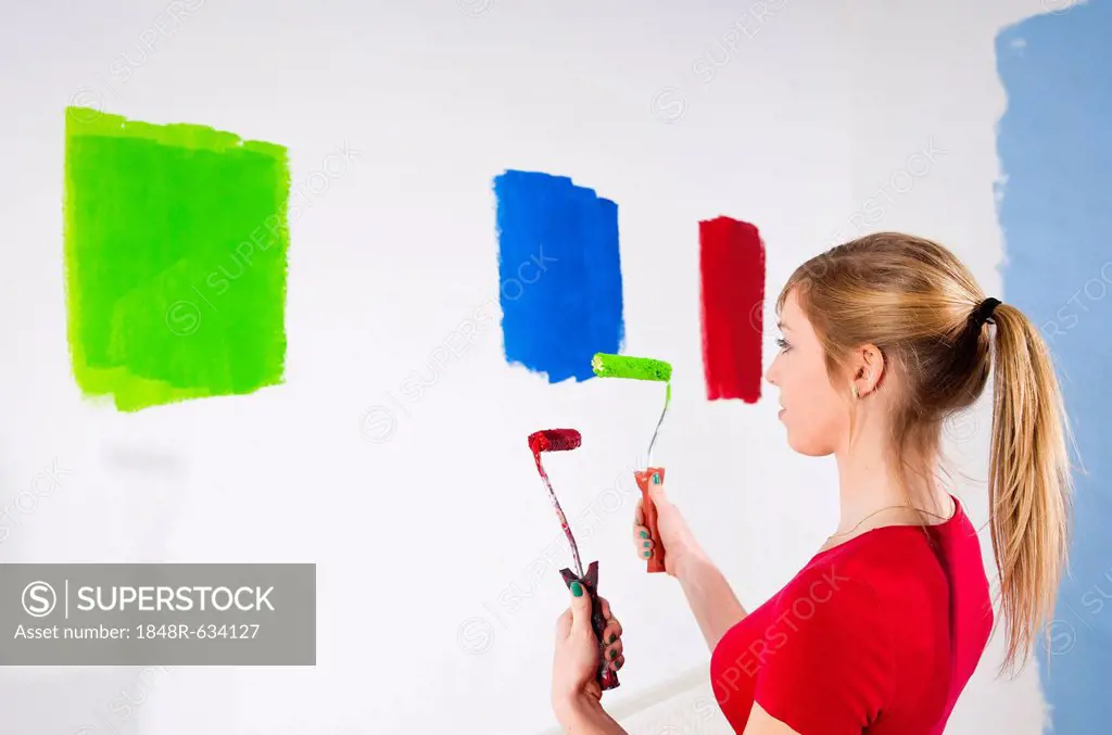 Young woman holding two paint rollers in front of a wall with paint samples