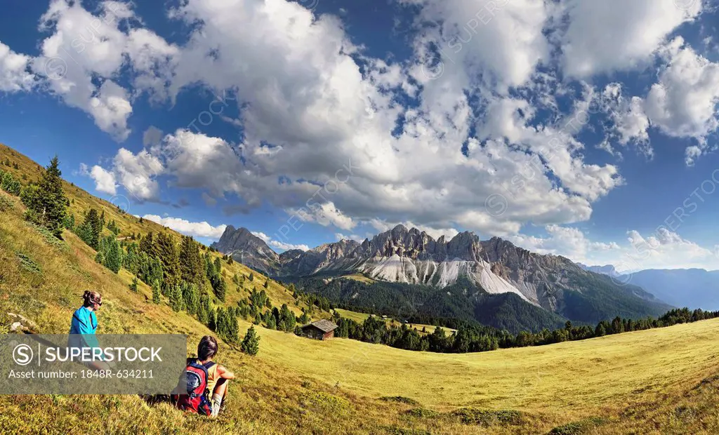 Hikers sitting near Enzianhuette mountain lodge on Plosen mountain, enjoying the view of the Afer Geisler group and Peitlerkofel mountain, Wuerzjoch r...