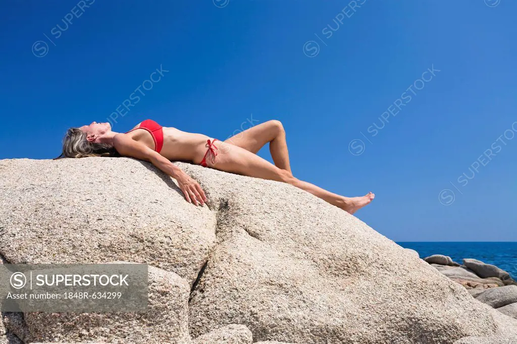 Woman sunbathing on the rocks of Palombaggia beach, south-east coast, Balagne region, Corsica, France, Europe