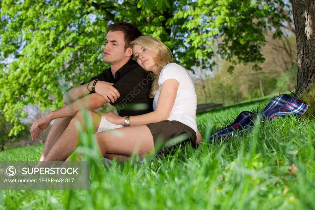 Young couple sitting on a picnic blanket under a tree in a park in spring
