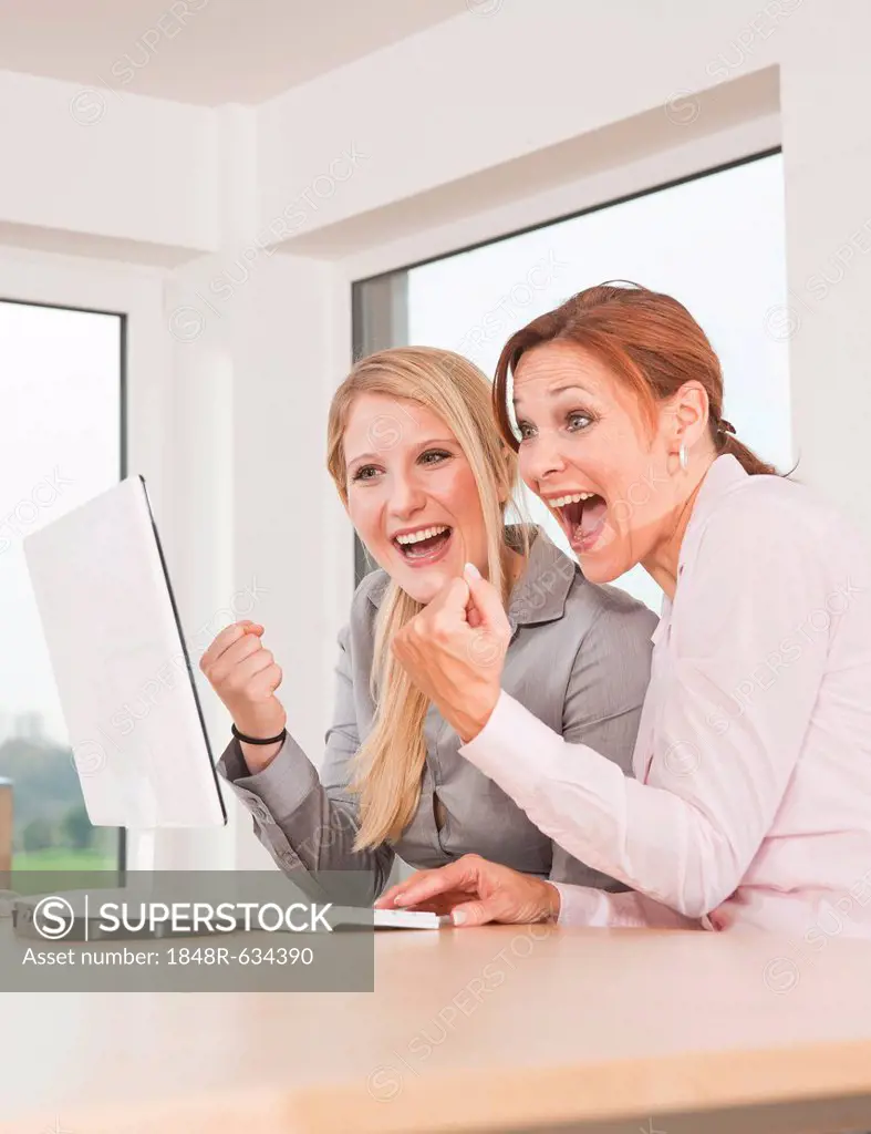 Two women cheering while sitting in front of a computer