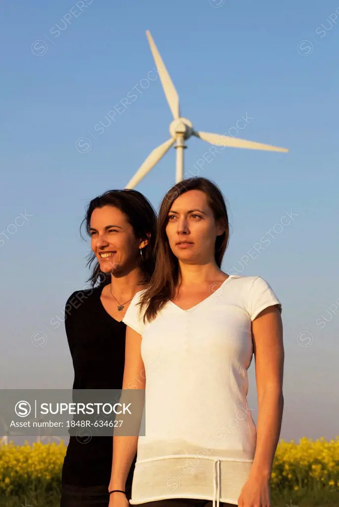 Two women in front of a canola field and a wind turbine