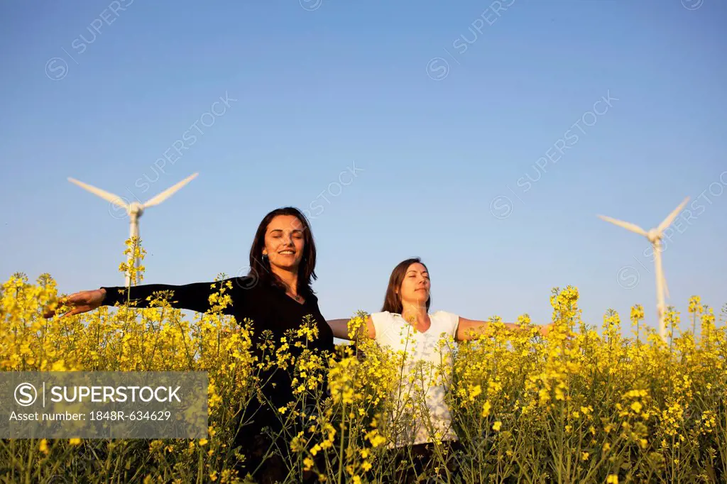 Two women in a canola field in front of a wind turbine