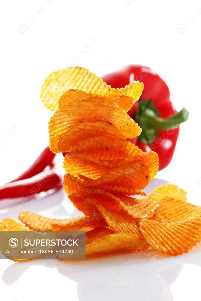 Paprika potato chips stacked in front of a capsicum and chili peppers