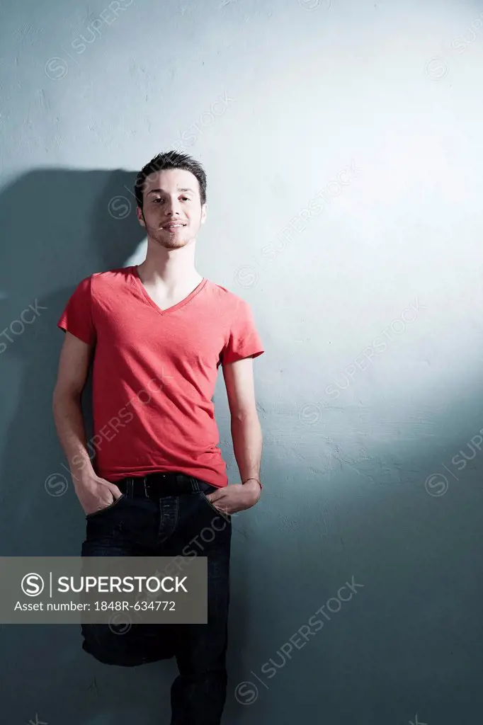 Cool young man leaning against a wall, smiling