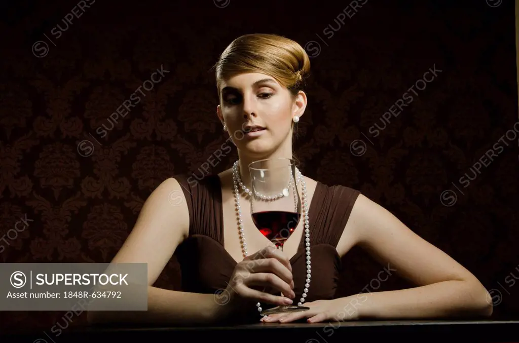 Young woman wearing a pearl necklace and pearl earrings, with red wine in a wine glass