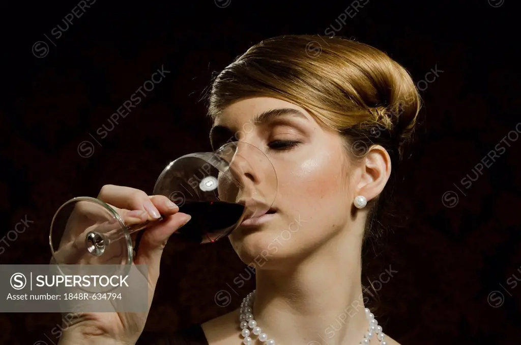 Young woman wearing a pearl necklace and pearl earrings, drinking red wine in a wine glass