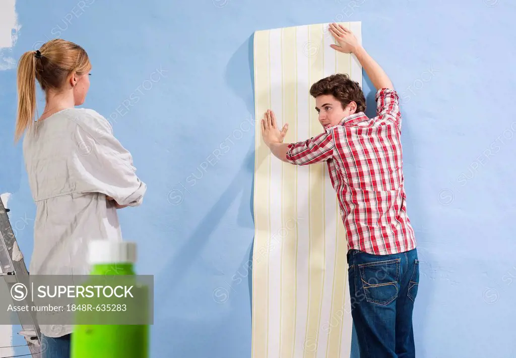 Young couple applying wallpaper to a wall