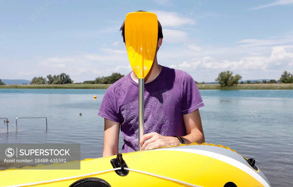 Young man holding paddle of rubber dinghy in front of his face, having fun boating, transition of Lake Constance into Seerhein river and Untersee lake...