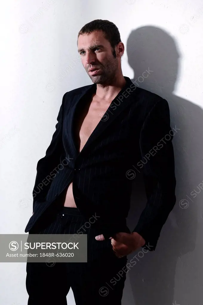 Man, 37 years, wearing a suit without a shirt, leaning against wall