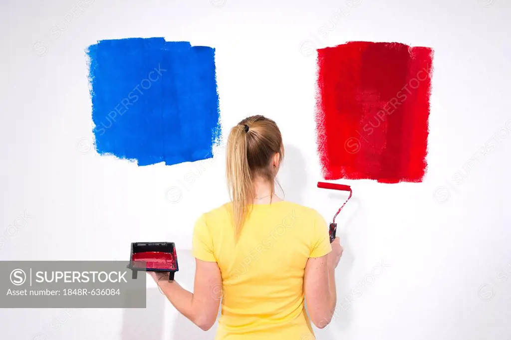 Young woman standing with a paint tray and a paint roller in front of a wall with paint samples