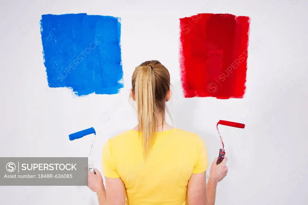Young woman standing with two paint rollers in front of a wall with paint samples