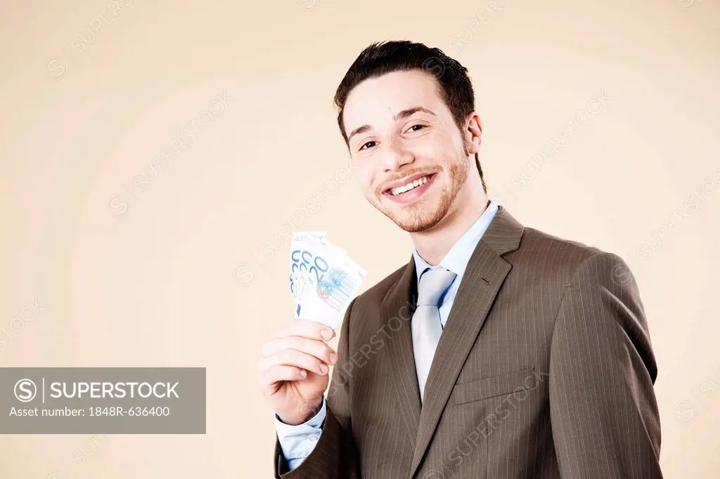 Smiling businessman holding a fan of 20-euro banknotes in his hand