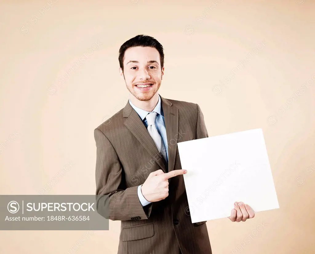 Young man wearing a suit pointing to a blank board in his hand