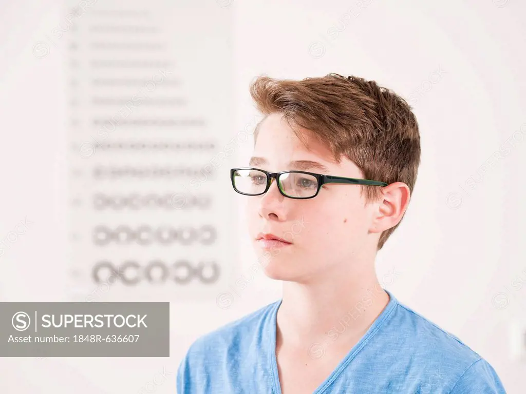 Teenage boy wearing glasses standing in front of an eyesight test