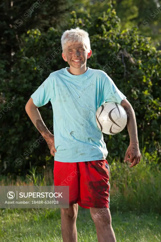 Portrait of a dirty, smiling boy with a football under his arm