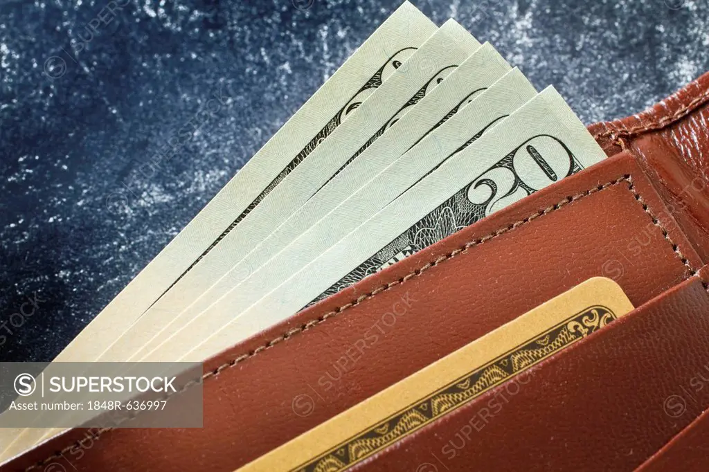 Close up of a leather wallet with the tips of five 20 dollar bills sticking out