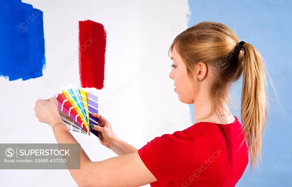 Young woman holding colour cards in front of a wall with colour samples