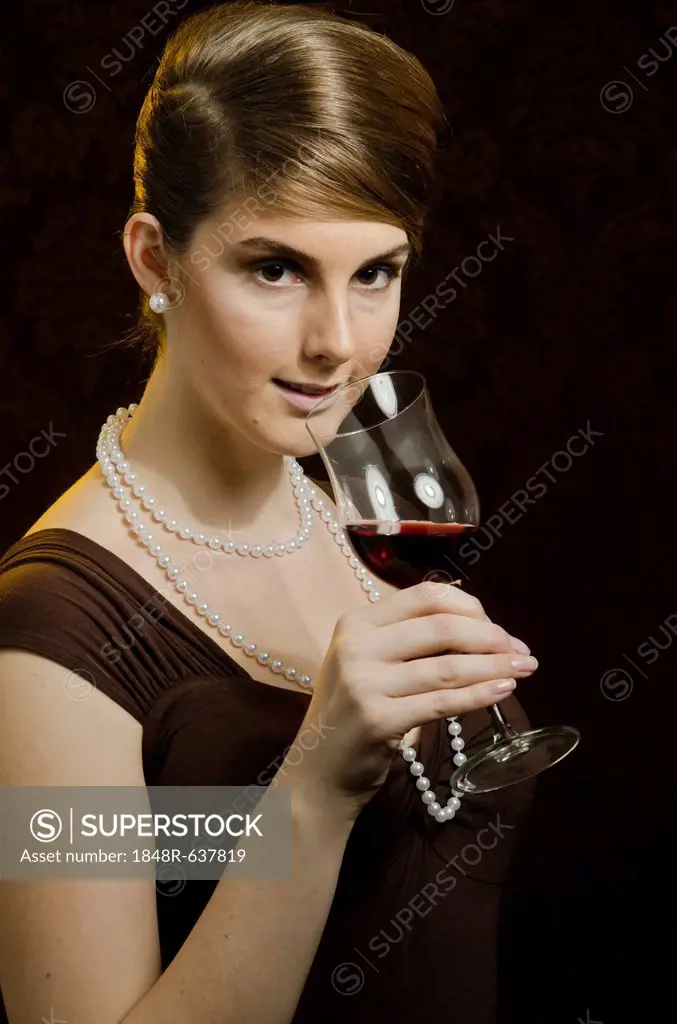 Young woman wearing a pearl necklace and pearl earrings, drinking red wine in a wine glass