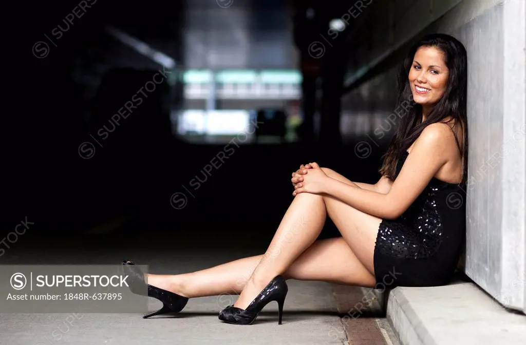 Young woman with long dark hair, short dress and high heels posing sitting