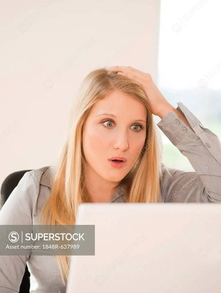 Young woman working on computer, shocked, surprised