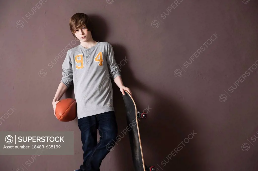 Cool boy holding a football and a skateboard