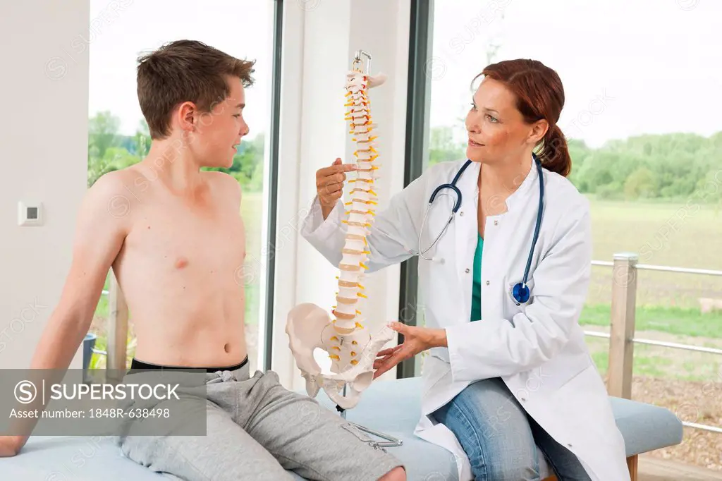 Orthopedic surgeon explaining a model of the spine to a teenage boy
