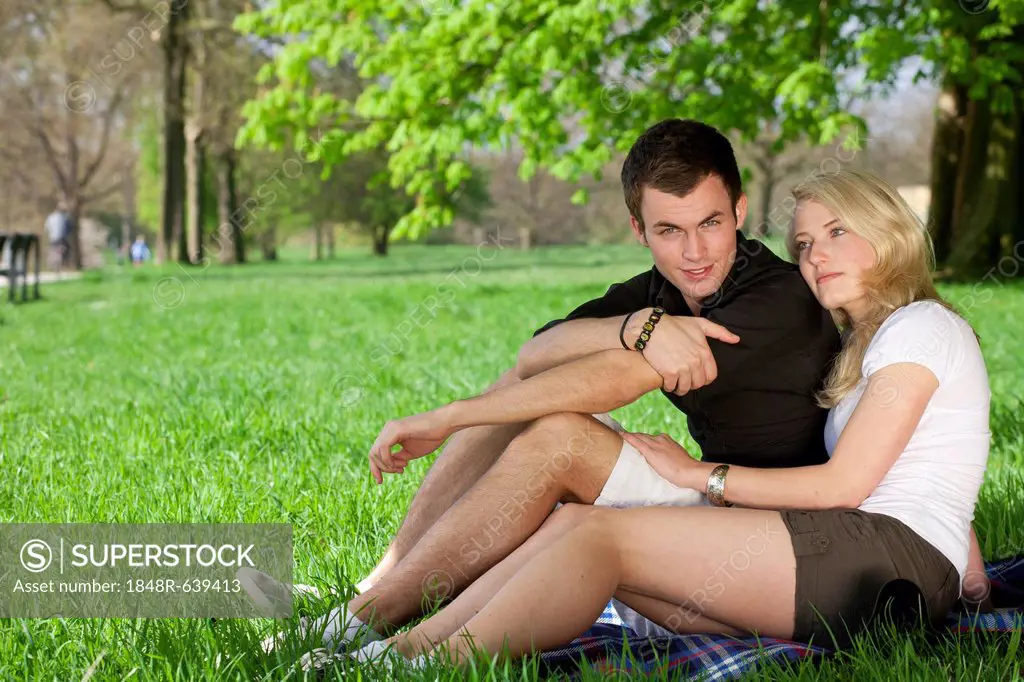 Young couple sitting on a picnic blanket under a tree in a park in spring