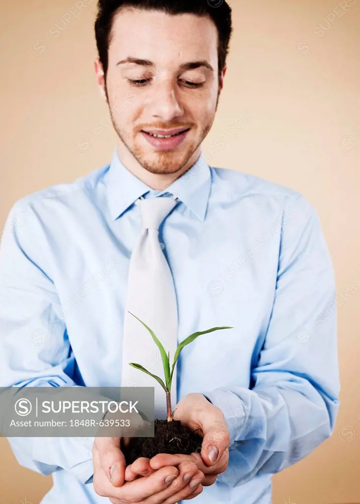 Smiling young manager holding a plant in his hands